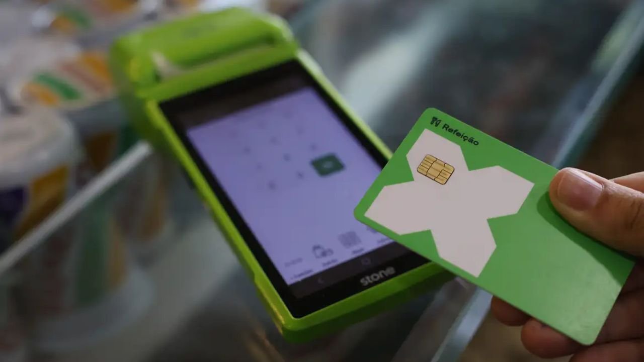 Cartão de vale-alimentação sendo utilizado em máquina de pagamento; novas regras do PAT entram em vigor.